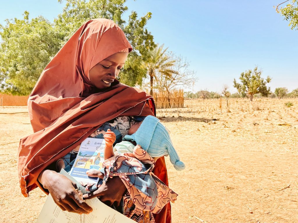 Woman holds baby and brochure from New Incentives, in Kano State, Nigeria.