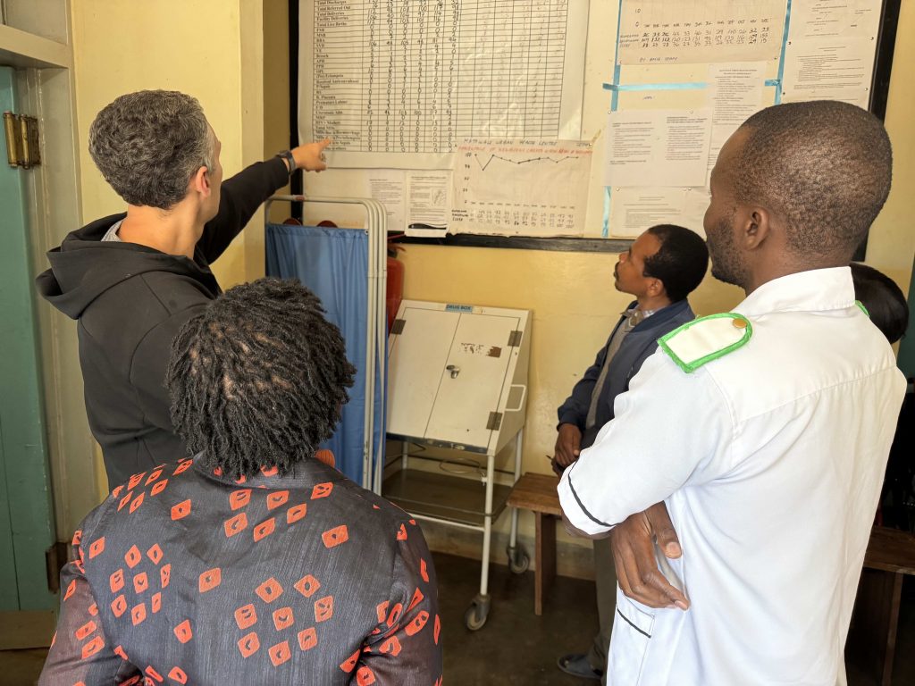 Photo of GiveWell CEO Elie Hassenfeld pointing at chart with health data on wall in Malawi.